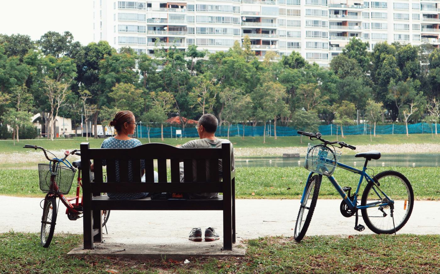 man and woman sitting on bench near two bikes viewing green field during daytime by Nguyen Thu Hoai courtesy of Unsplash.