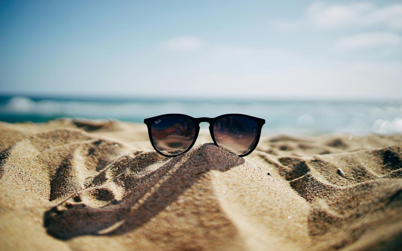 black Ray-Ban Wayfarer sunglasses on beach sand by Ethan Robertson courtesy of Unsplash.